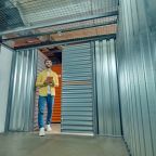 Inspection of garage. Young adult affable man with tablet entering clean empty garage in storage premise looking up with interest