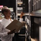 Police investigator studying archival crime case materials, working overtime in detective office room. African american policewoman searching evidence records and taking file from shelf SSUCv3H4sIAAAAAAAACmyRwW7bMAyGX8XQOSpkWbFl3wr0sFsDrLus2YGS6FitYxmynGII8u6jnPS2k8gf5E/x45UZWLxl3ZX5cVyXFCH5MLFO7FjEyWHcwkusarFF4LcHnU8hehi3zECywwRnZN20juNtx5YEaV1wIWPKLCQ8UfmWf098v2addYxR+WpycNv9R/tDQ0842b/Zi8wijgib9Tsry7qtdYtc4V5xpTVy7Zzi2qiqRmtA90BWQvfCIjbcOFNx1YLgIK3ksuwdtI3sm0pSGThbO+M0r3q750rinspKwYWSZdO62tRaM/rO51fCeH7sBqvzIa91CRZGEqss+hkifJfM0Vs/ne5JSEOGSouGdUqRtmJlo2j6GMIMZiSGPfngjg2wLFTjHkLmSAcK57vPFFJmwKjTEd5sU1WqbvaN1EqrWraqzBS3QwyeGvOs3Emh/fTu8TlP/kwRLnBGcSFLSTBLx4FocoEC9qqHvsLMcZ3HAC7ldamzD/G8HSvCQkC2FQjBDGkg8Xd3PB5+vL69Ho/lU/Fr6yQIxWEIKSwkCkH621connviA1PxfMZ7cMAwj1jw4gUT2uQvWPzEtPm8hAnvvbxpZPX0MZ/Y7R8AAAD//wMAw8nvFcUCAAA=