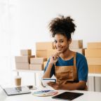 Startup small business SME, Entrepreneur owner African woman using smartphone or tablet taking receive and checking online purchase shopping order to preparing pack product box.