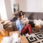 Smiling young couple move into a new apartment, sitting in the living room eating and taking a break from unpacking.